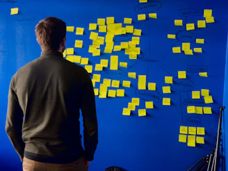 A person in a green sweater looking at a blue wall with yellow sticky notes