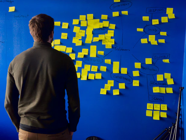 A person in a green sweater looking at a blue wall with yellow sticky notes