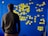 A person stands facing a blue wall covered with numerous yellow sticky notes arranged in a flowchart-like pattern. The notes are organized into categories with handwritten titles like 'Environment', 'Society', and 'Healthcare'.