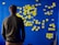 A person stands facing a blue wall covered with numerous yellow sticky notes arranged in a flowchart-like pattern. The notes are organized into categories with handwritten titles like 'Environment', 'Society', and 'Healthcare'.