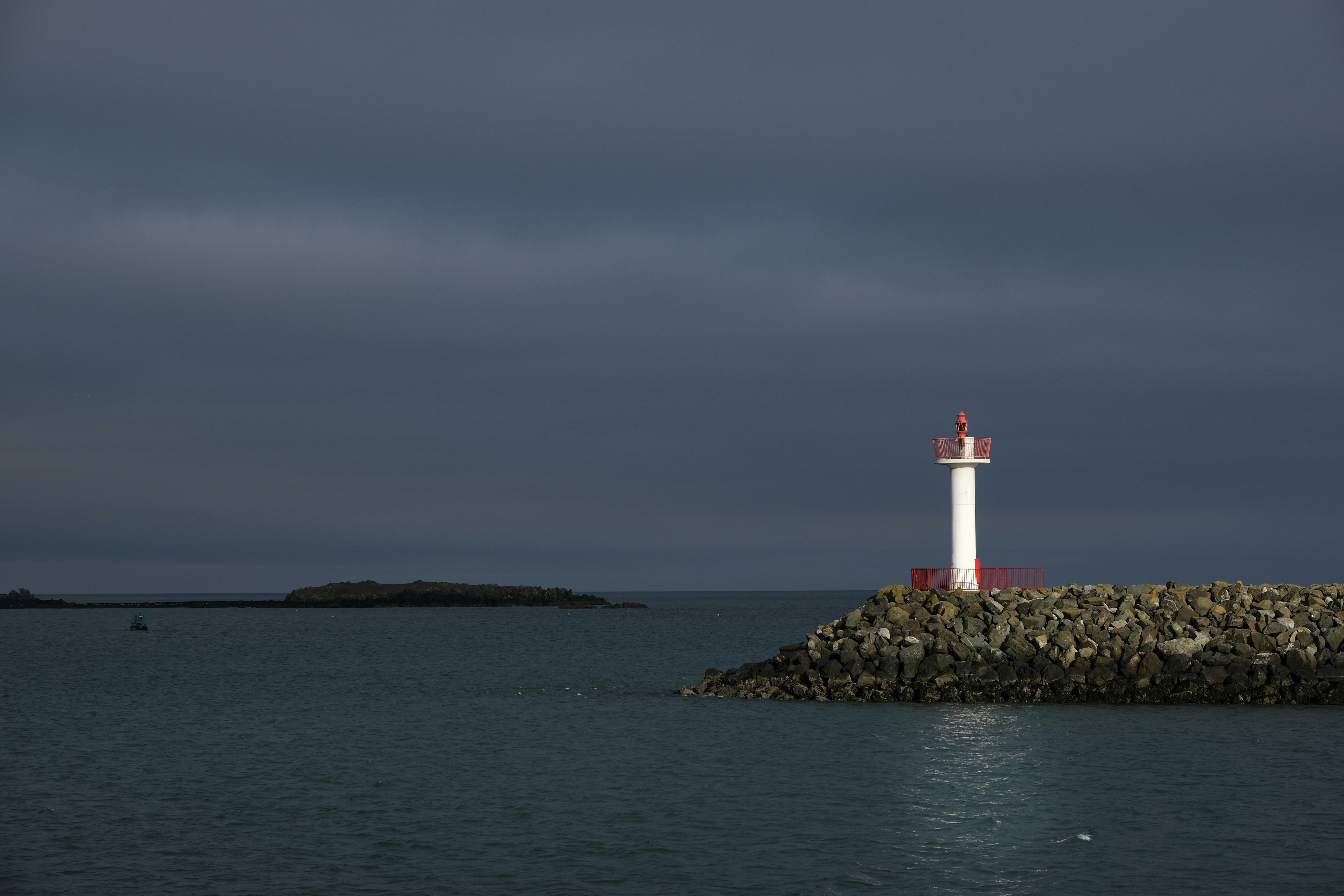 white and red lighthouse on brown rock formation near body of water during daytime