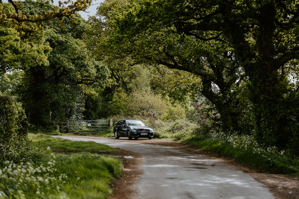 black car on road between green grass and trees during daytime