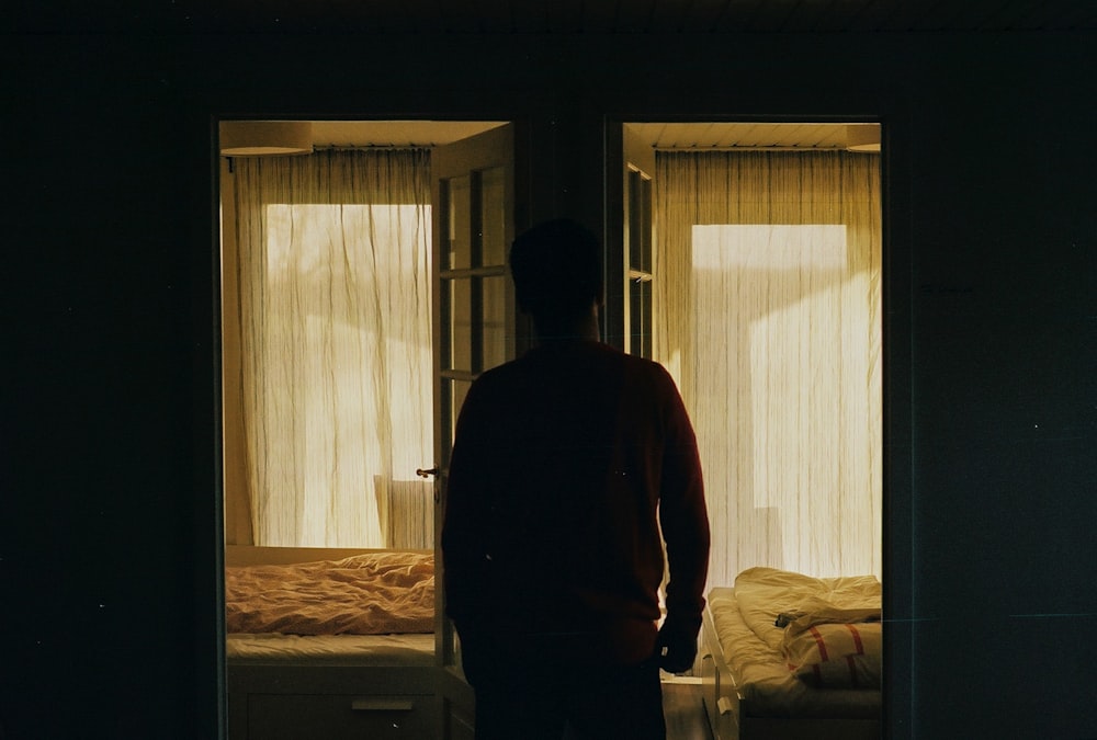 man in red long sleeve shirt standing near window