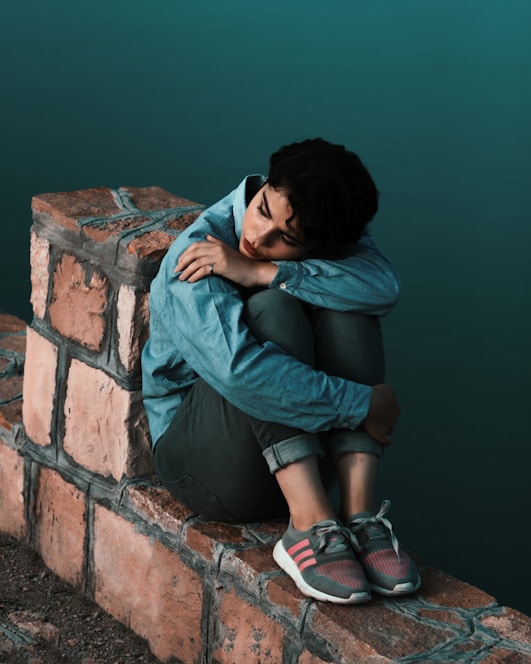 woman in blue long sleeve shirt and black skirt sitting on brown brick wall