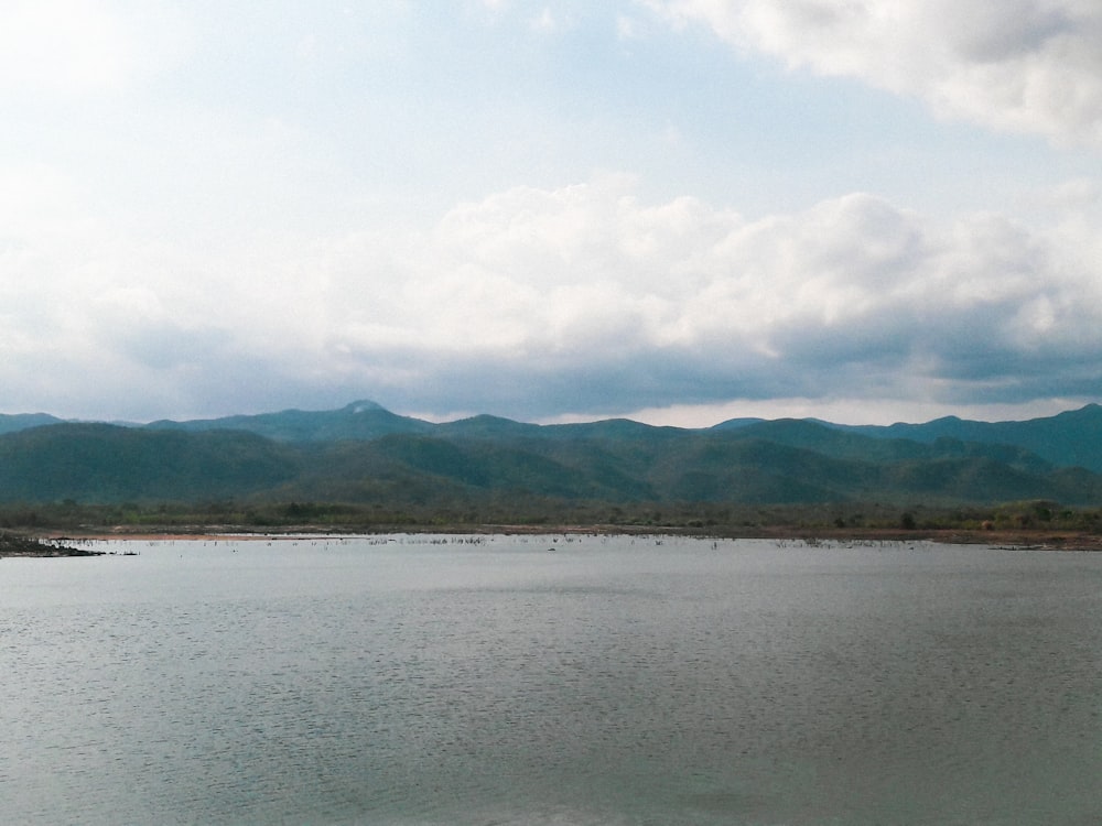 body of water near mountain under white clouds during daytime