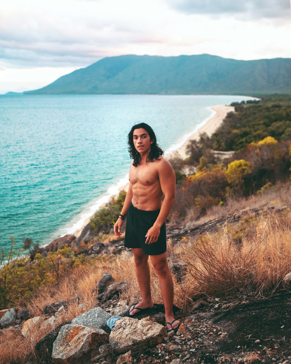 woman in black shorts standing on rock near body of water during daytime