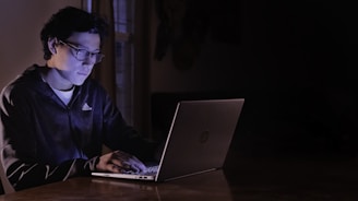 A focused professional working intensely on a laptop in a dark, stylish office environment.