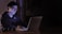 A focused individual studying stock market charts on a laptop in a dimly lit room.
