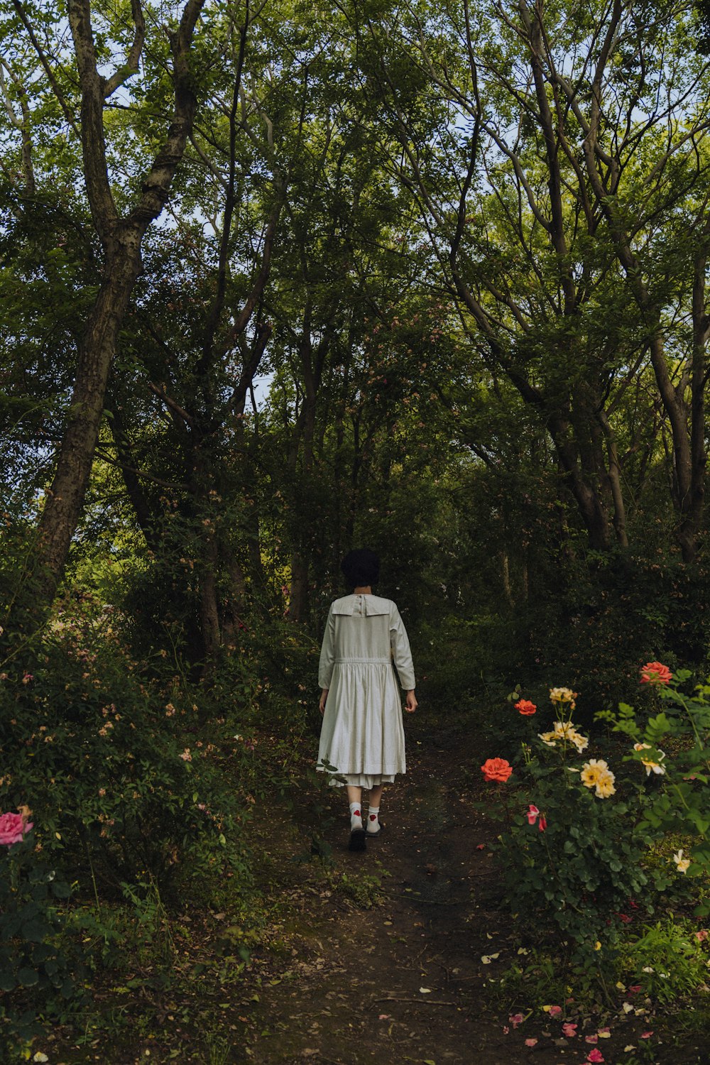 woman in white dress walking on pathway surrounded by trees