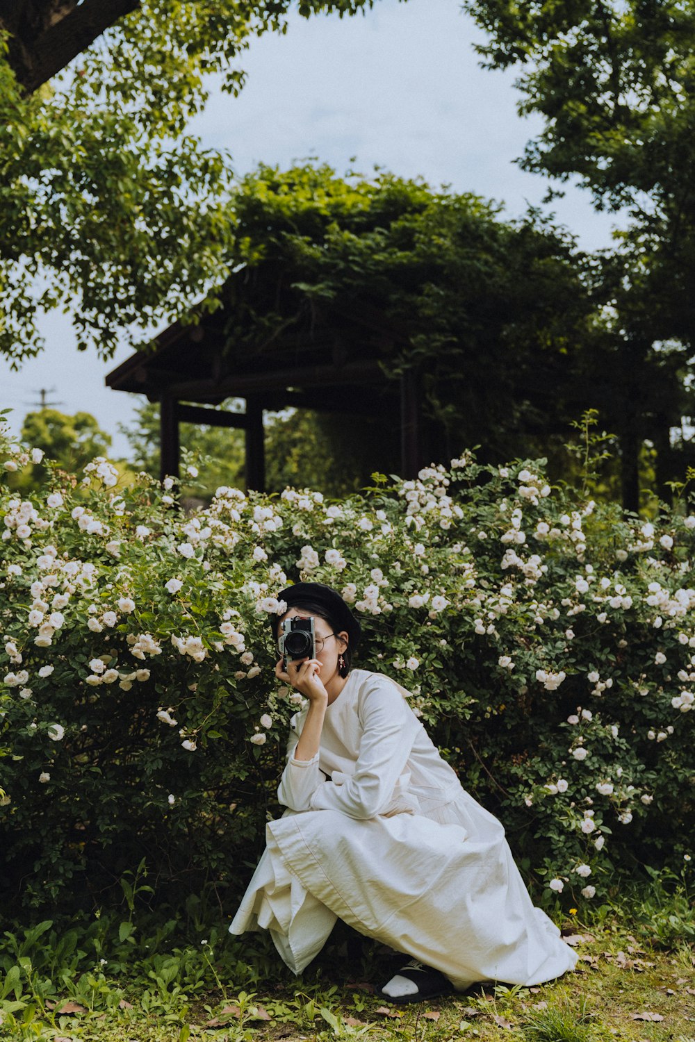 낮 동안 녹색 나무 근처에 서 있는 검은 선글라스를 쓴 흰색 드레스를 입은 여자