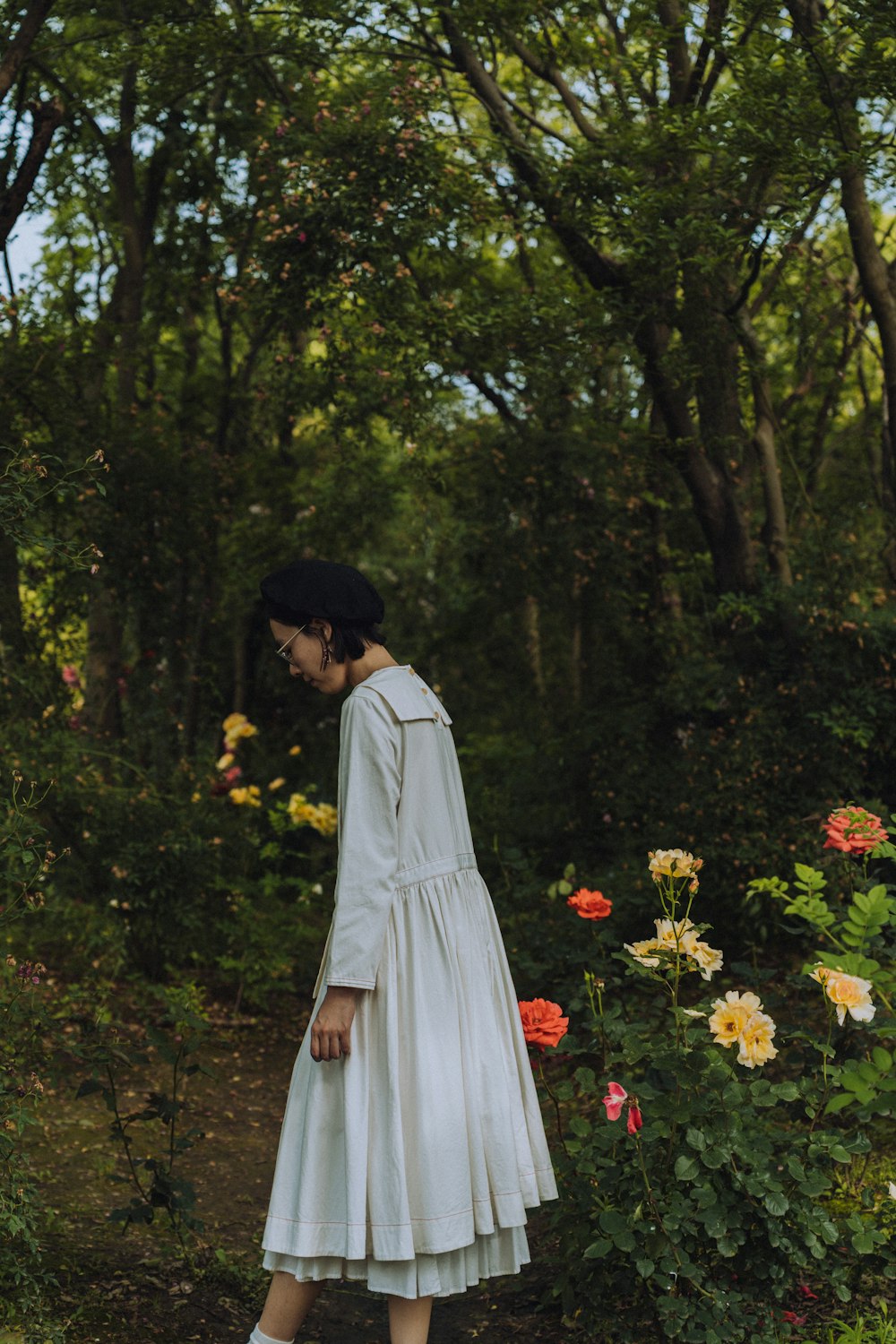 woman in white dress standing on green grass field surrounded by green trees during daytime