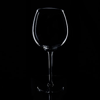 A wine glass is delicately outlined against a stark black background. The lighting accentuates the elegant contours and curves of the glass, creating a dramatic and sophisticated silhouette.