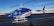A blue and white helicopter is parked on an asphalt runway. The helicopter has 'PIPE SURVEY' written on its side, with additional text that includes 'LASEN' and 'N284CA'. The background features a clear blue sky and snow-covered mountains in the distance.