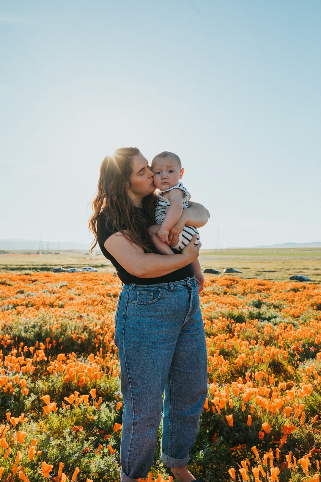 woman in black tank top carrying baby in white shirt on flower field during daytime