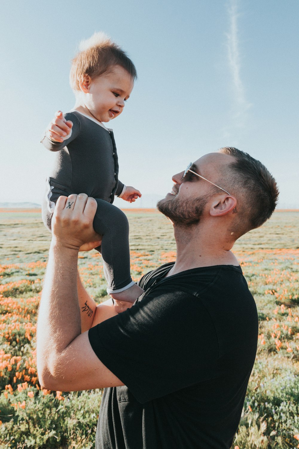 man in black tank top carrying baby in black onesie during daytime