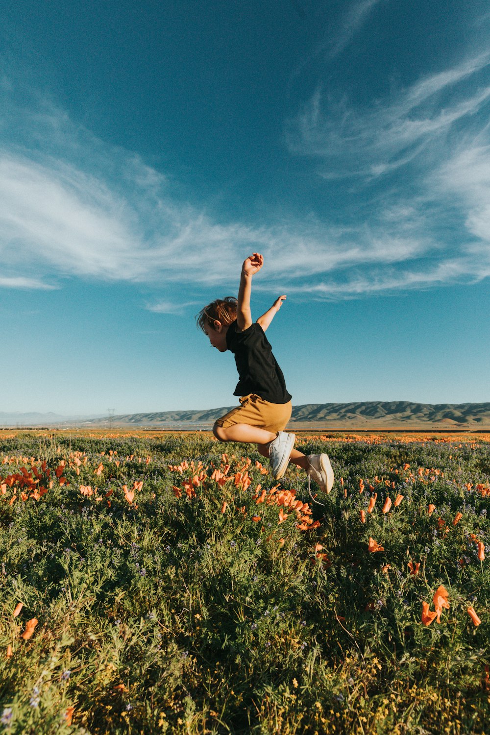 woman in black t-shirt and white pants standing on flower field under blue sky during