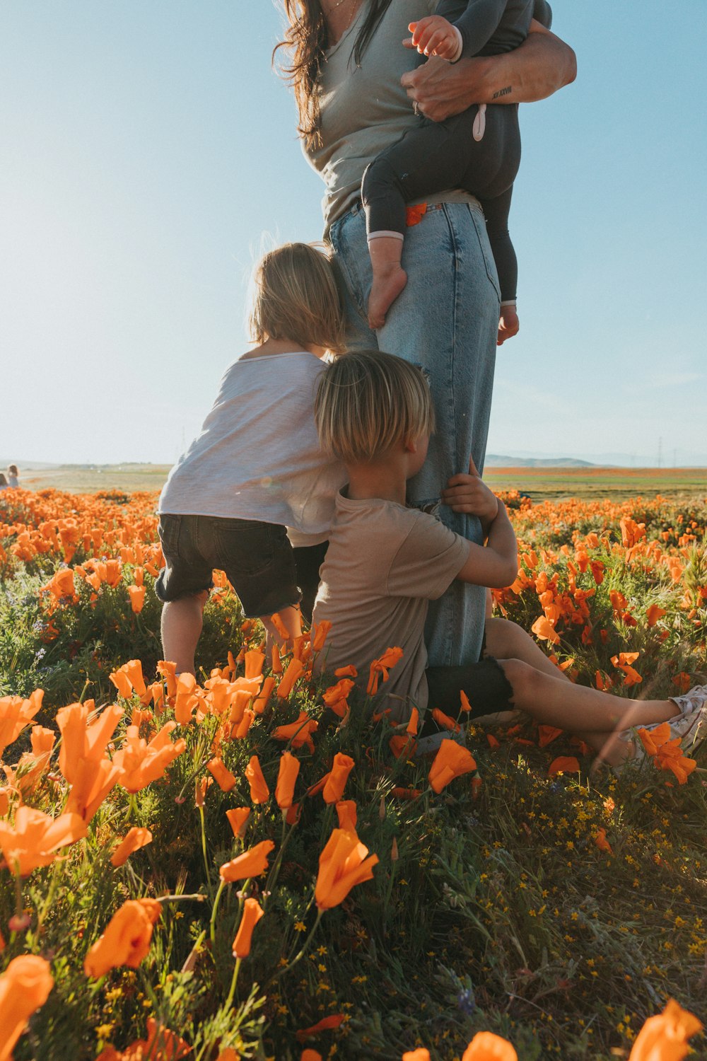 woman in white shirt carrying girl in black shirt on orange flower field during daytime