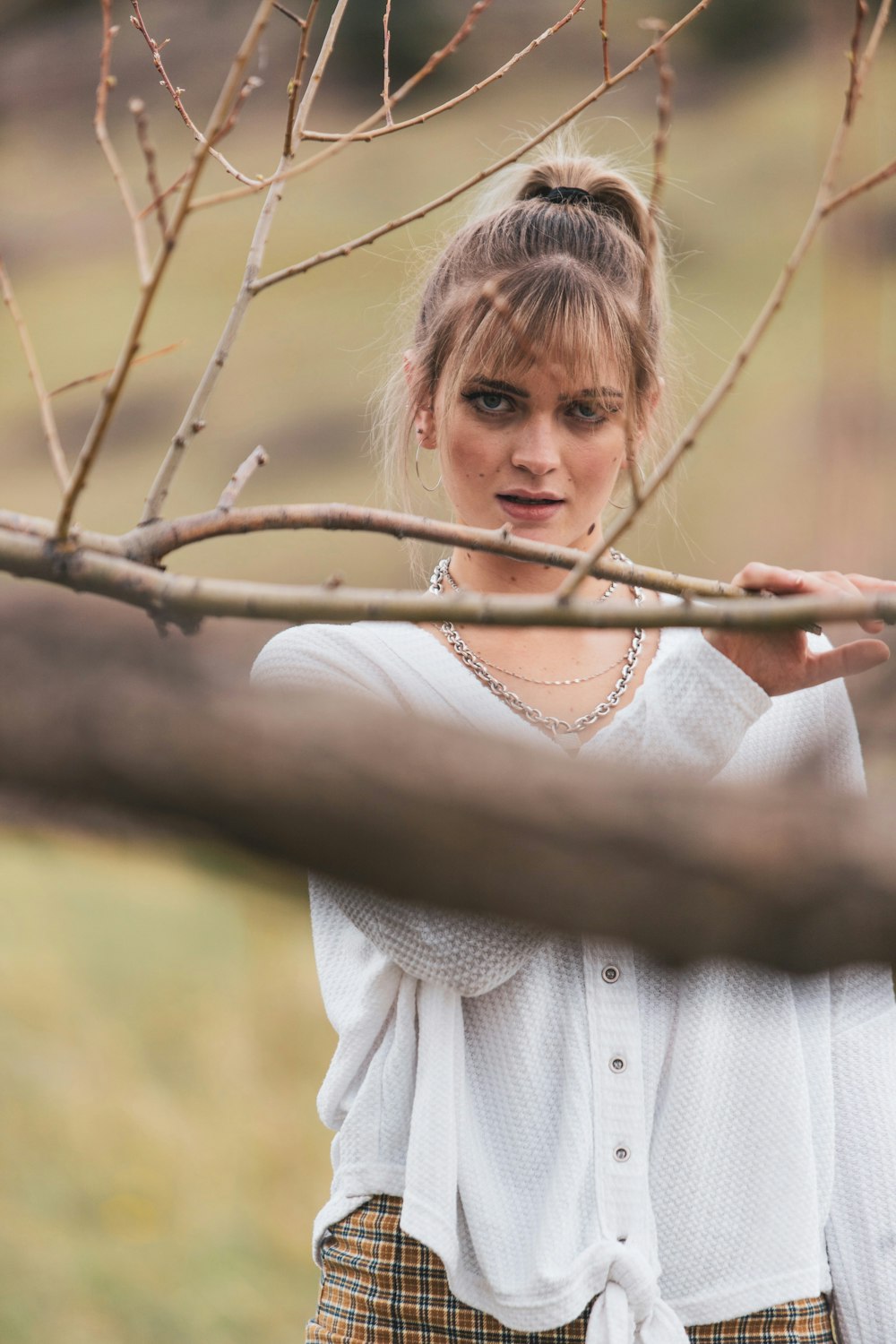 girl in white knit sweater standing on brown tree branch during daytime