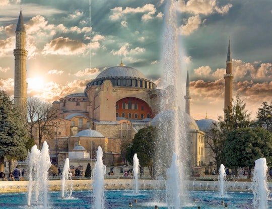 fountain in front of brown concrete building under cloudy sky during daytime in Hagia Sophia Museum Turkey