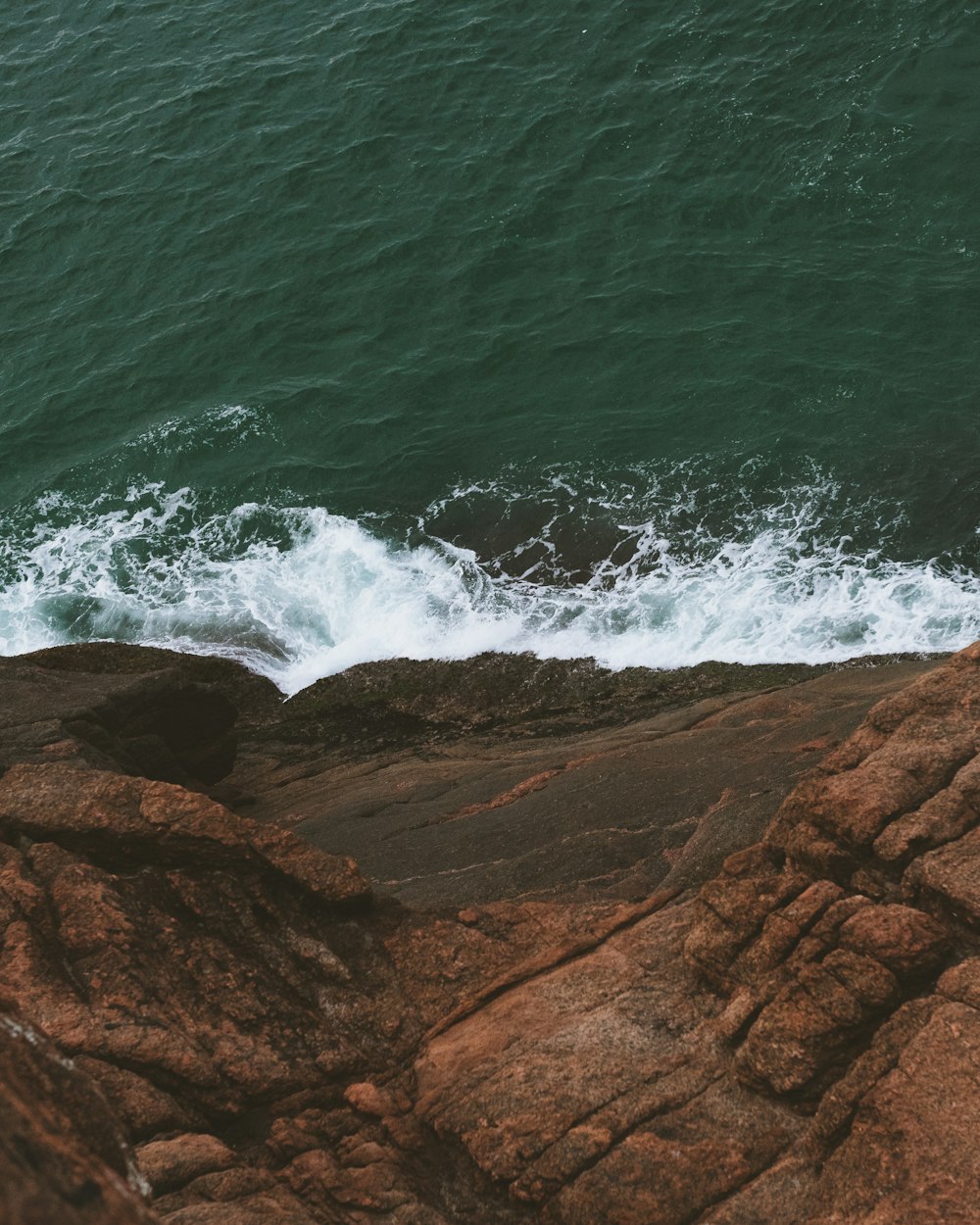 ocean waves crashing on brown rocky shore during daytime