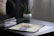 Bright studio shot of a digital art print resting on a sleek wooden desk next to a potted plant.
