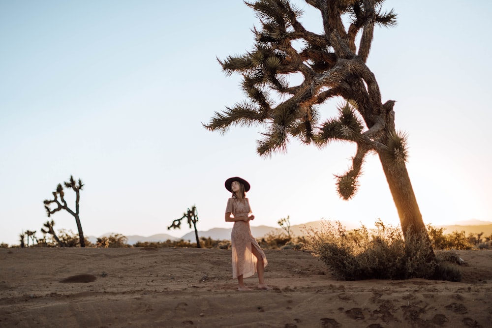 woman in white tank top and black sunglasses standing on brown sand during daytime