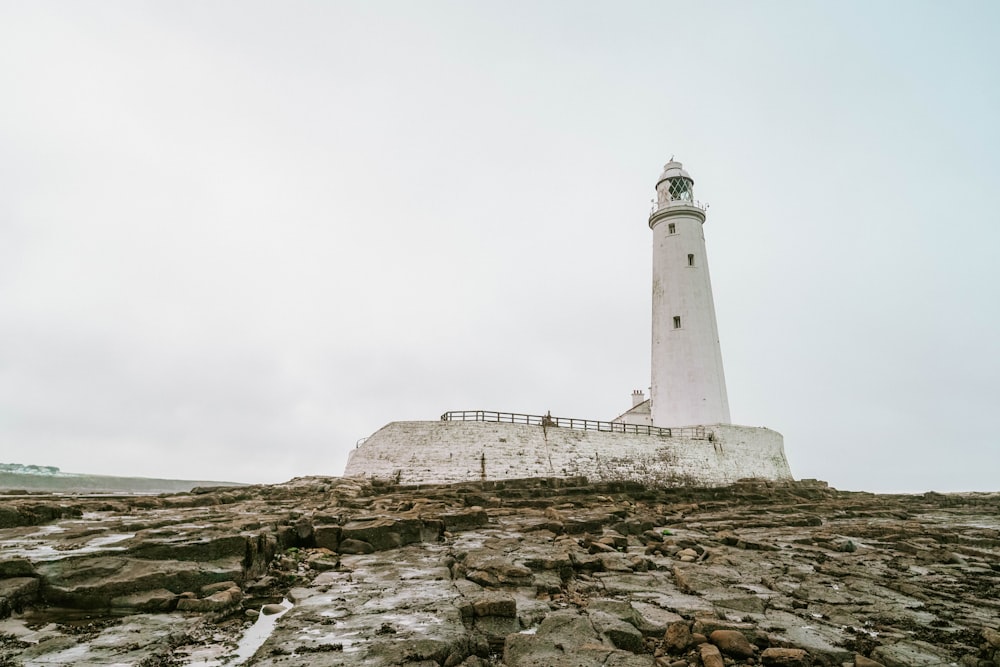 white lighthouse on rocky hill under white sky during daytime