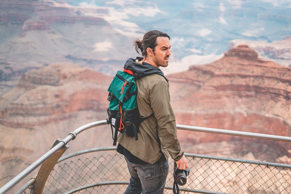 man in brown jacket and blue denim jeans standing on bridge during daytime