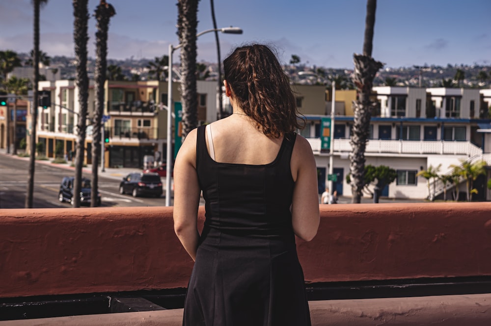 woman in black spaghetti strap dress sitting on brown wooden bench during daytime