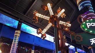 A futuristic amusement park ride is captured, with spinning mechanical arms decorated with lights. The ceiling features an illuminated space pattern, adding to the sci-fi theme. Colorful pillars and gears contribute to the mechanical, industrial vibe.