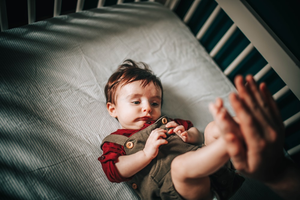 baby in gray shirt lying on bed