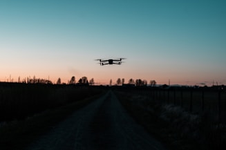 white drone flying over the road during sunset