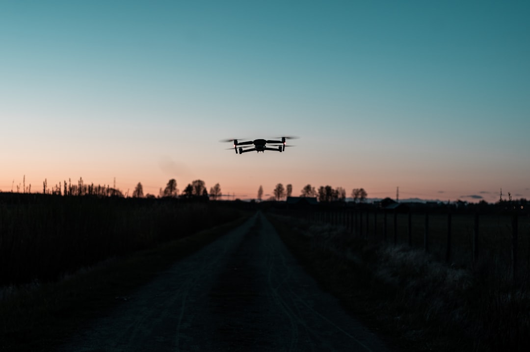 white drone flying over the road during sunset