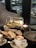A two-tiered serving platter featuring assorted sandwiches and pastries. There are two cups of cappuccino, each on a saucer with a spoon, all set on a sleek, dark table. The background is softly blurred, suggesting a cozy, modern setting.