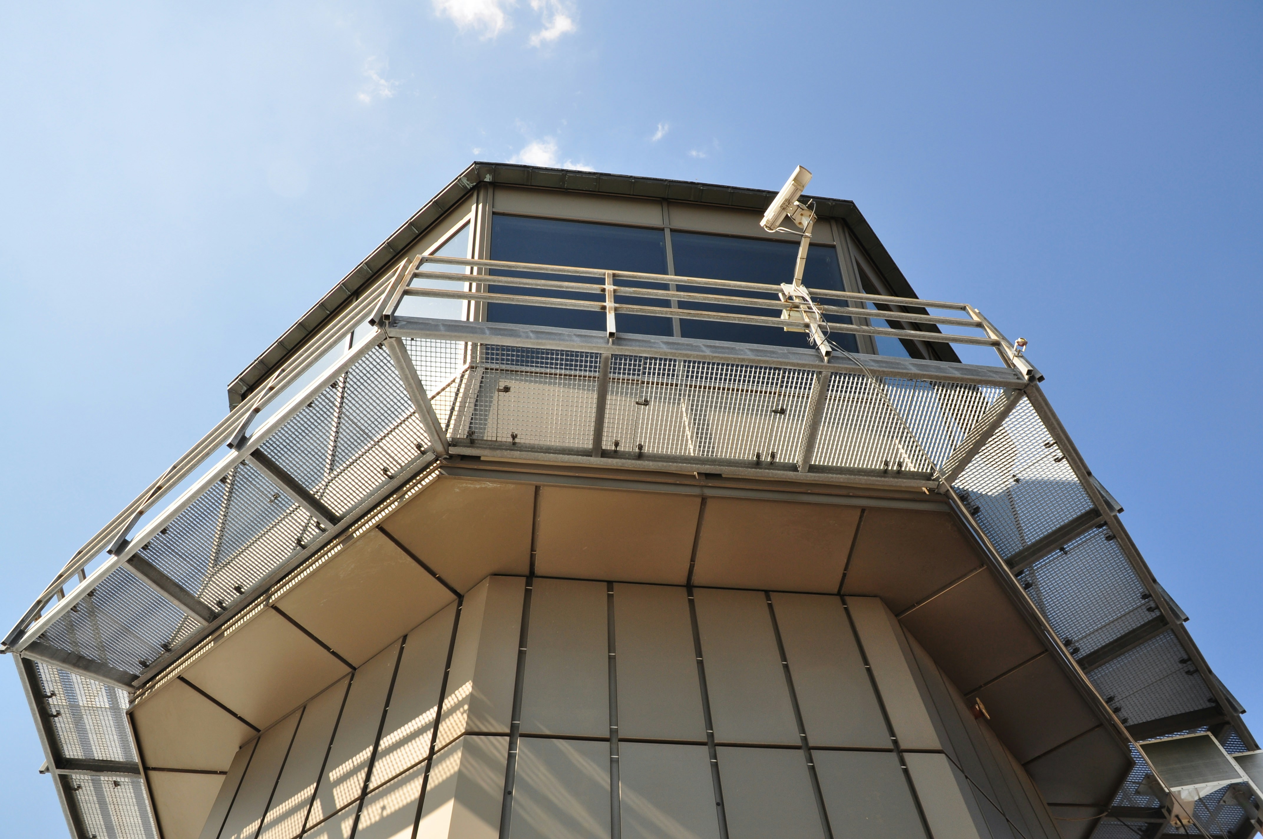 Airport surveillance using a security camera at a side tower building. The sharp contrast between the monotonous repetitive pattern of the tower building and the brightly blue colored sky. The surveillance camera in between is the subject of the picture.