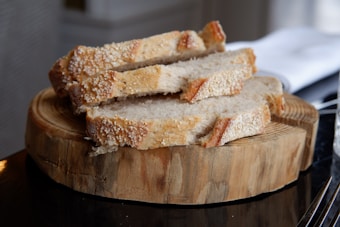 Slices of crusty bread arranged on a wooden cutting board with a rustic appearance. The bread has a golden-brown crispy crust and a soft, light interior. The image is captured in a natural light setting, suggesting a cozy and inviting atmosphere.