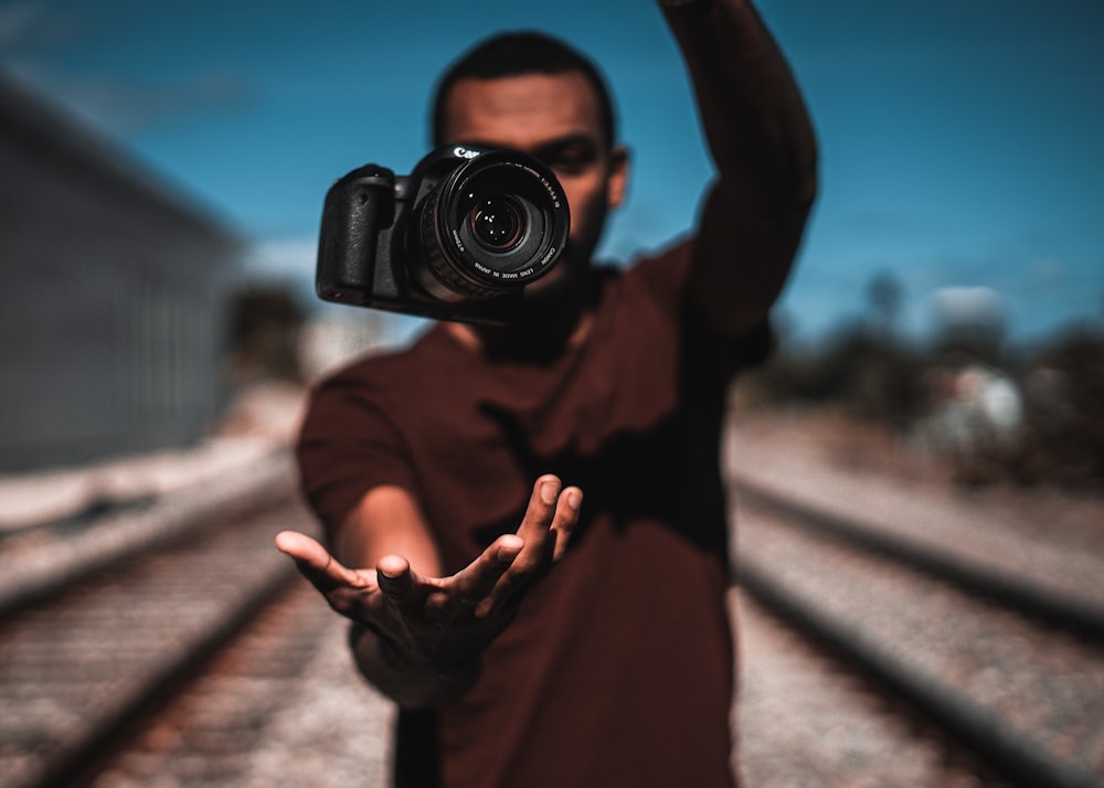 Persona con camisa marrón de manga larga sosteniendo una cámara DSLR negra