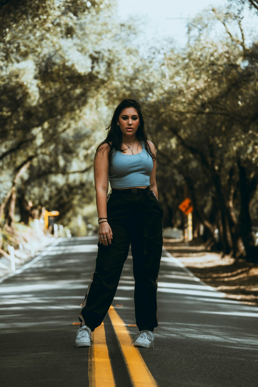 woman in white tank top and black pants standing on road during daytime