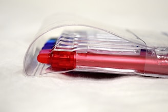 Several colorful pens encased in a clear plastic packaging, primarily showcasing a red pen in the forefront.