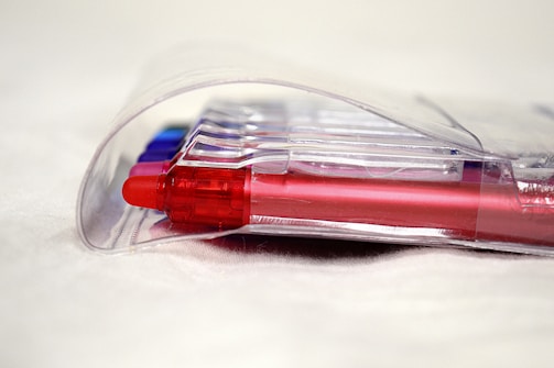 Several colorful pens encased in a clear plastic packaging, primarily showcasing a red pen in the forefront.