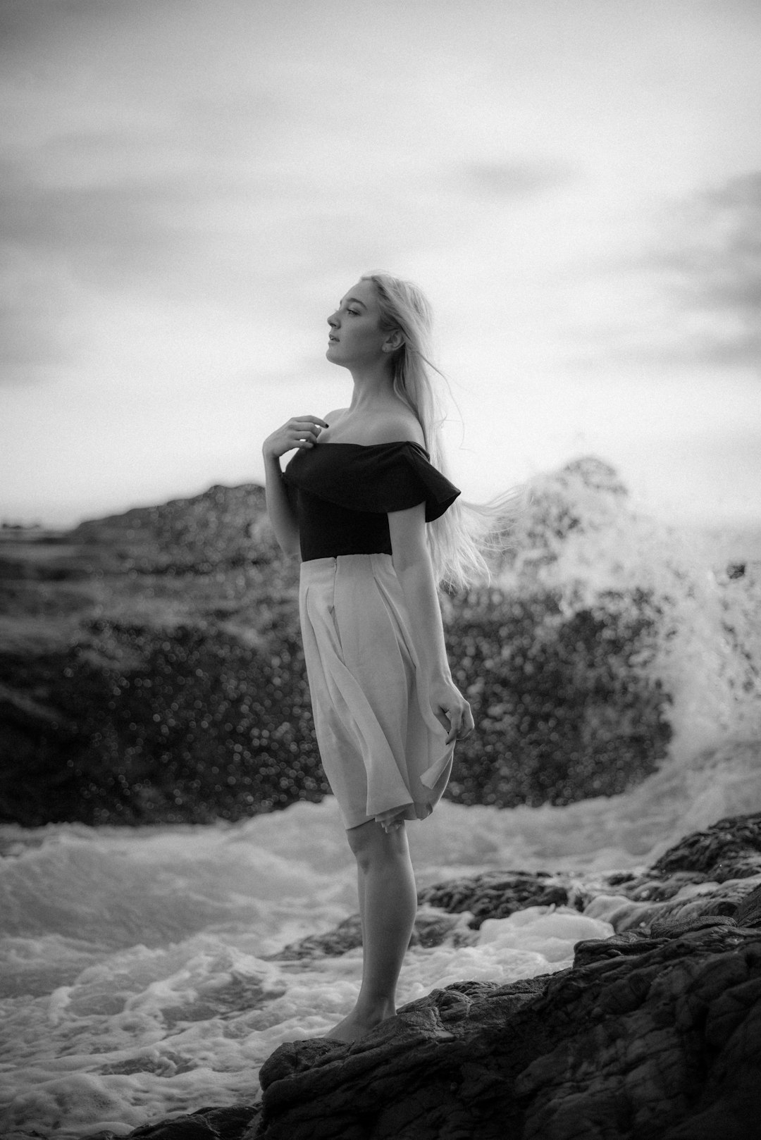 grayscale photo of woman in black tank top and skirt standing on rock