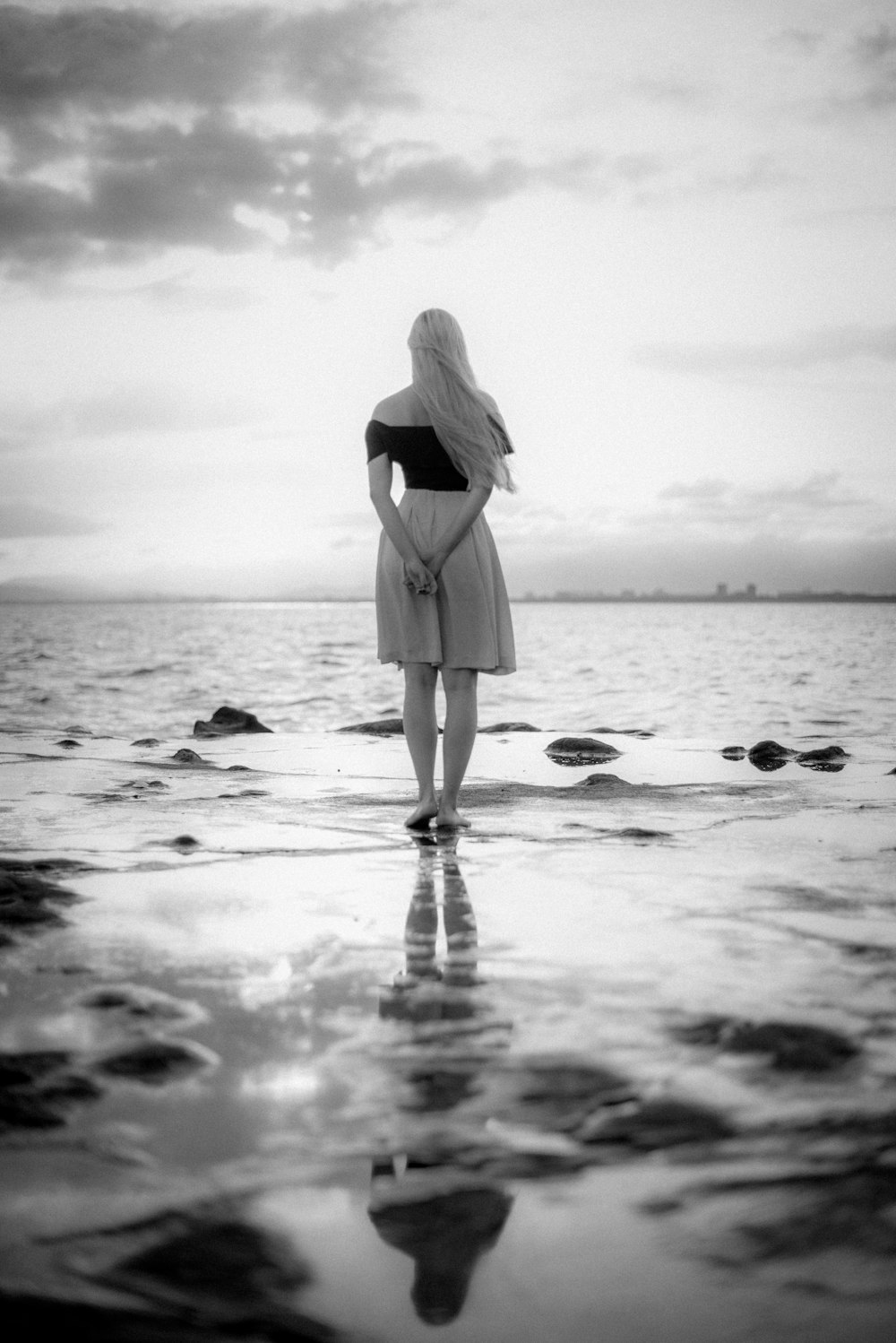 Frau in schwarzem Kleid am Strand stehend