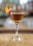 A warmly lit close-up of a classic Manhattan cocktail garnished with a cherry on a wooden bar counter.