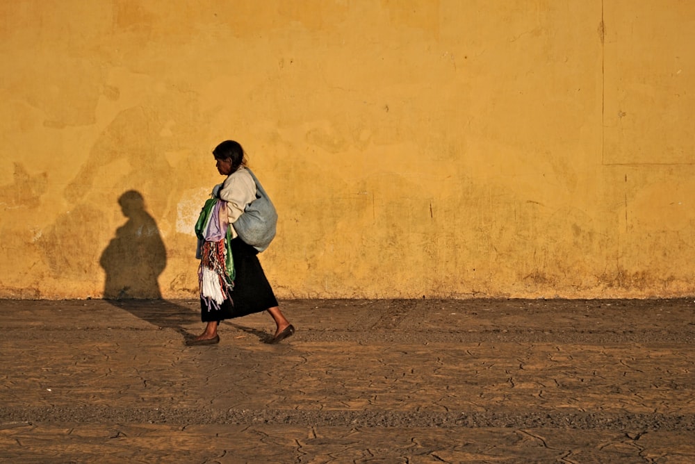 Mujer con camisa blanca de manga larga y falda negra de pie junto a la pared amarilla