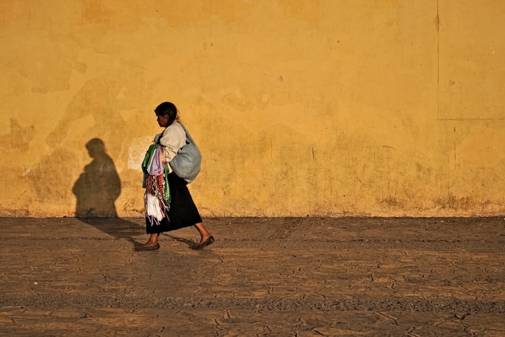 woman in white long sleeve shirt and black skirt standing beside yellow wall