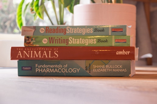 A stack of colorful books on a wooden table with a cozy reading nook in the background.