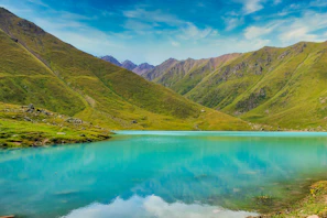 green mountains beside body of water under blue sky during daytime