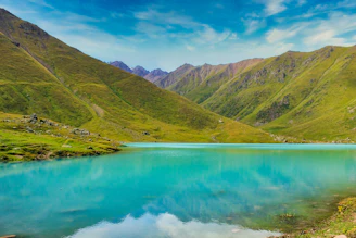 green mountains beside body of water under blue sky during daytime