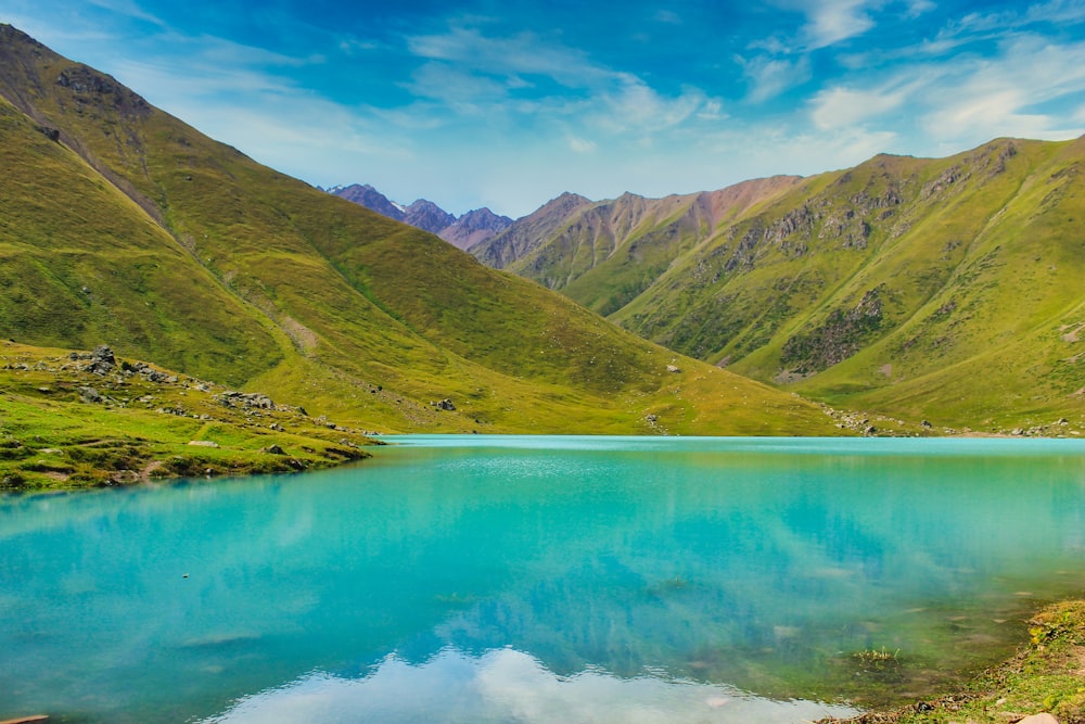 Grüne Berge neben Gewässern unter blauem Himmel tagsüber