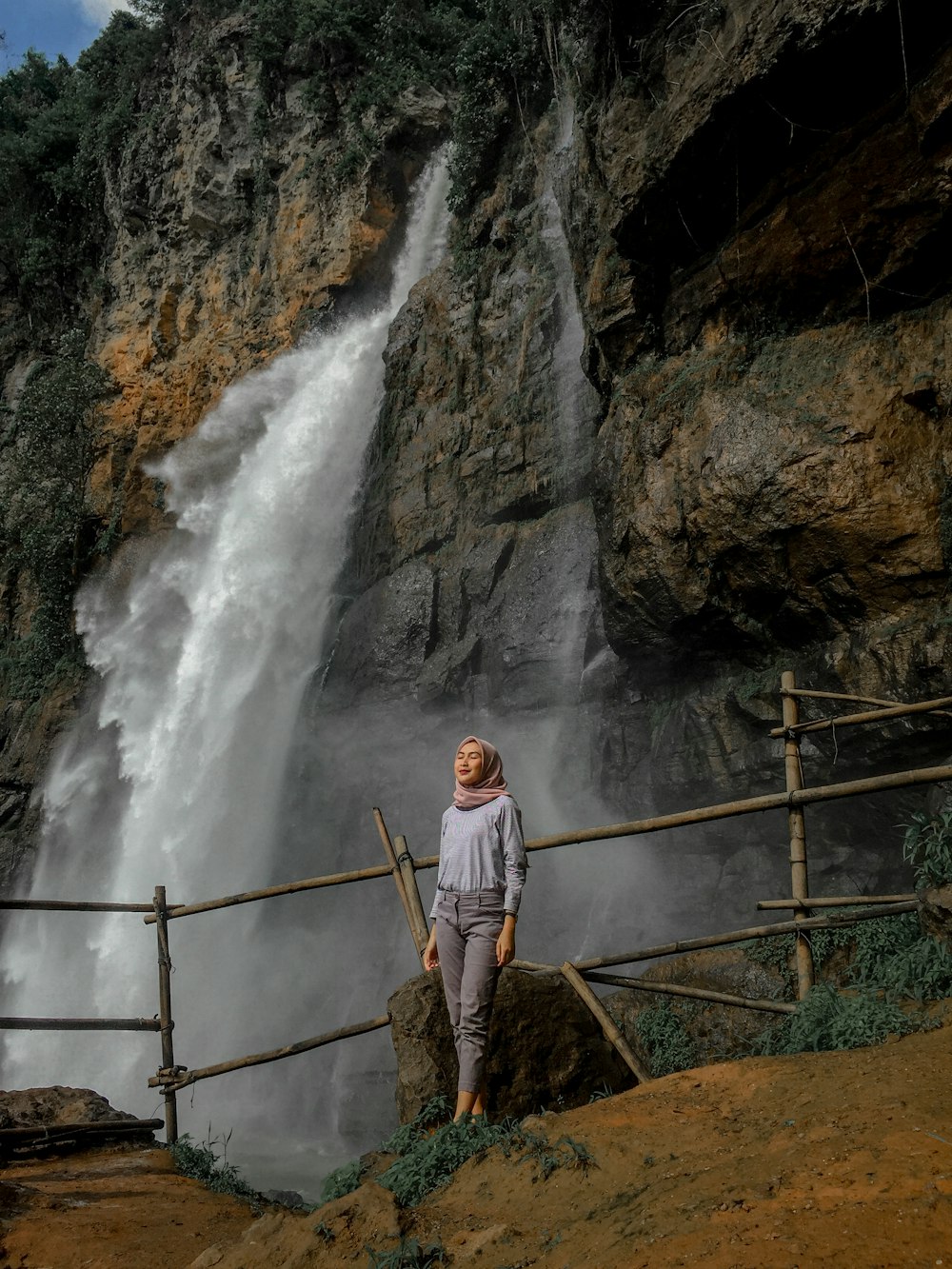 man in white long sleeve shirt and brown pants standing on brown wooden ladder near waterfalls